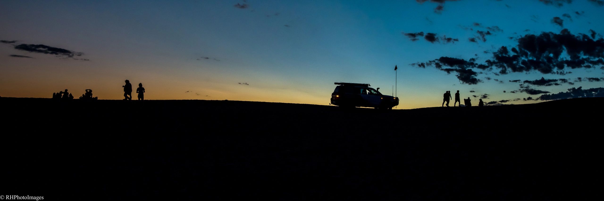 Silhouettes of people and a vehicle at sunset on a hill.