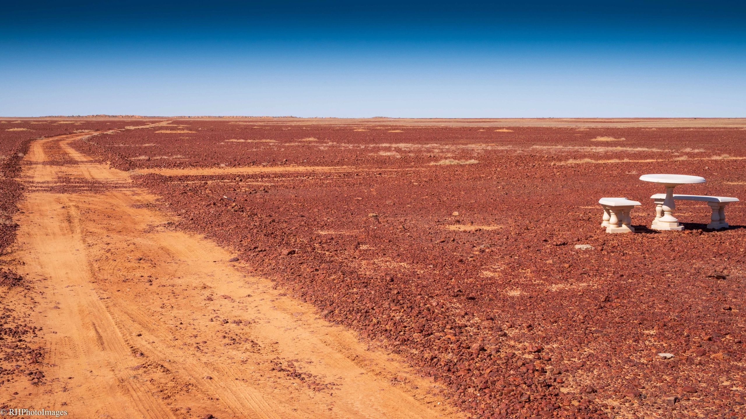 Desert landscape with a dirt road and a white stone table set.