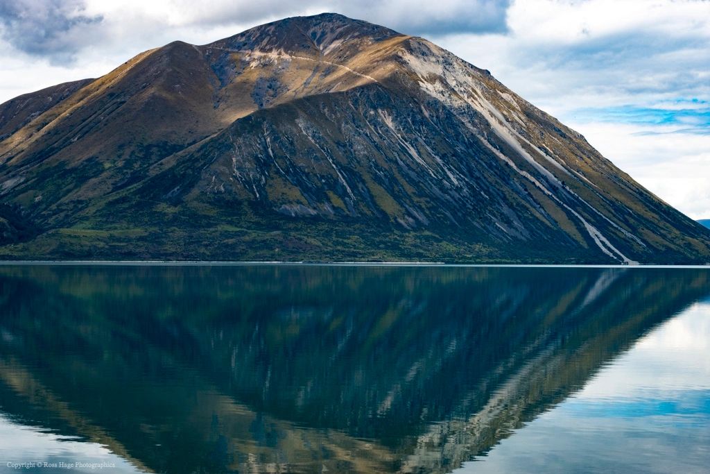 Mountain reflected perfectly in calm lake water under a cloudy sky.