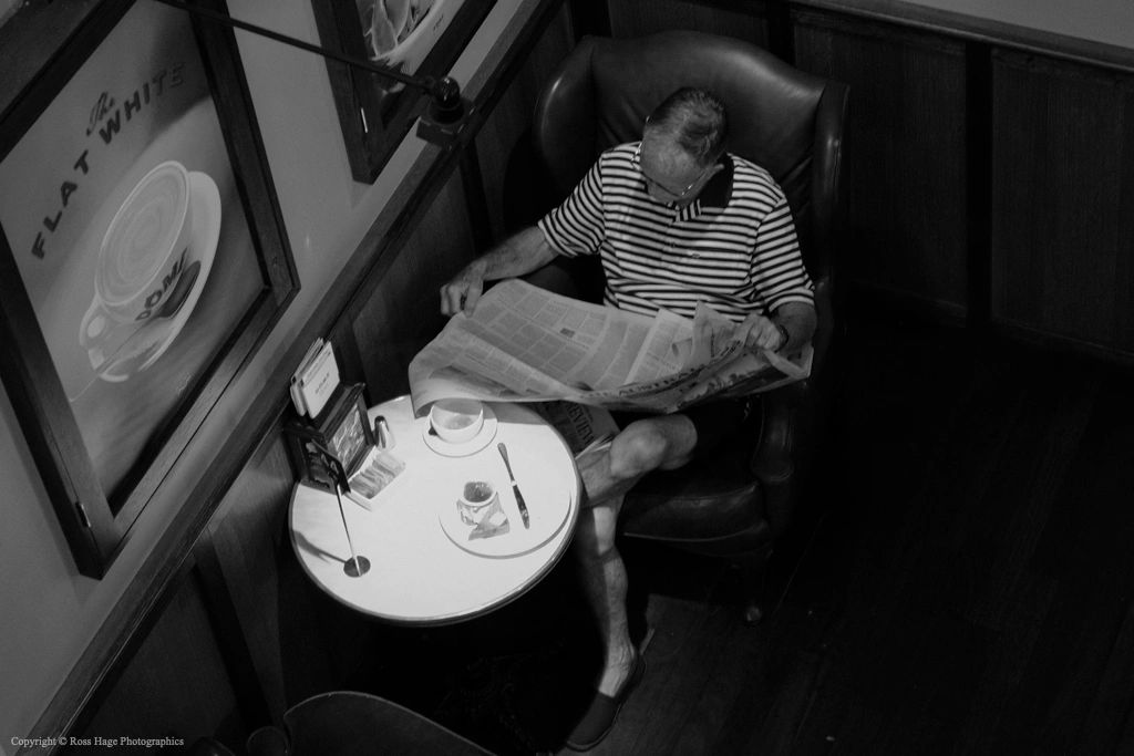 Man reading a newspaper in a cozy cafe corner, black and white.