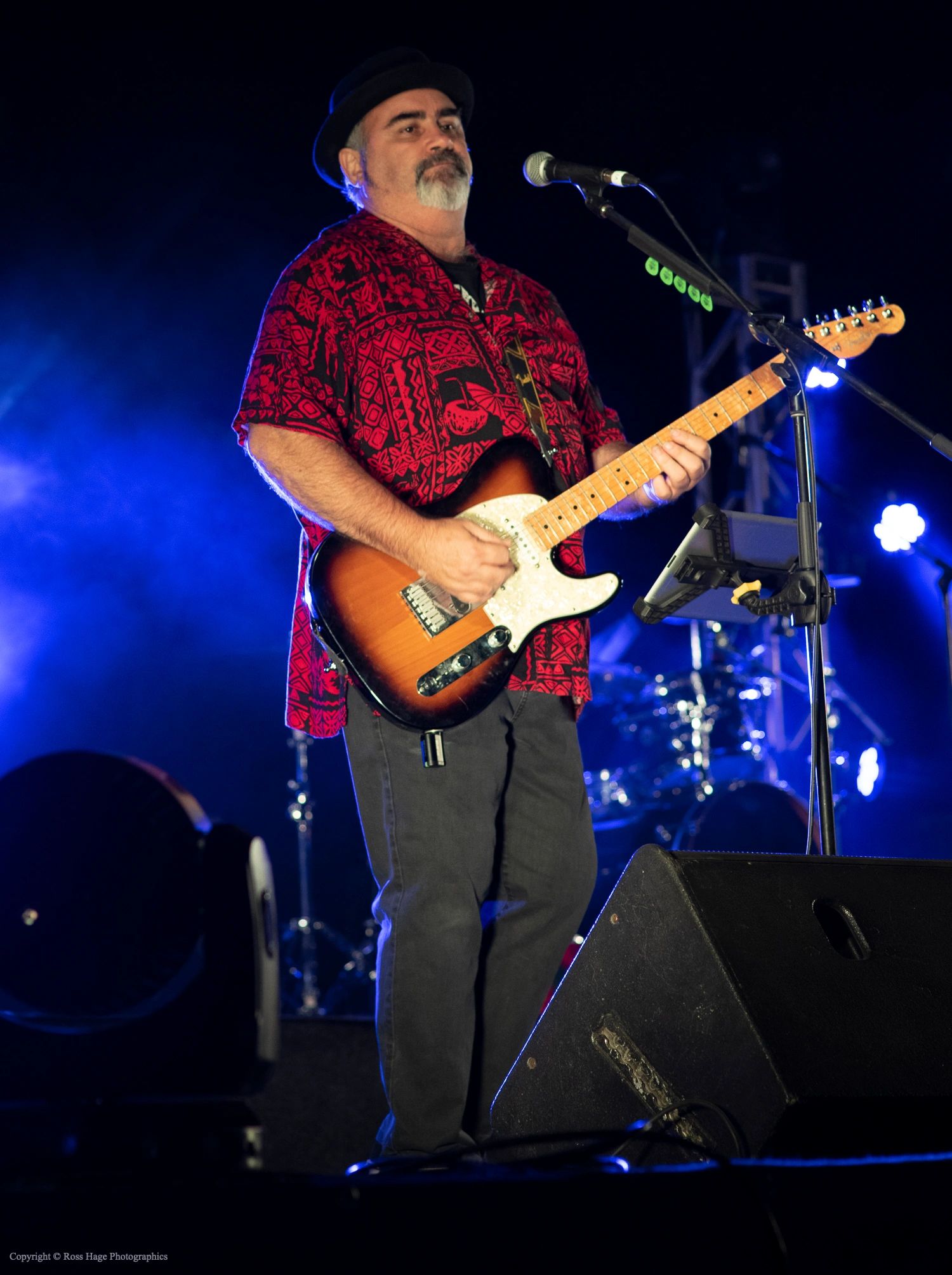 Man playing electric guitar on stage with blue lighting.