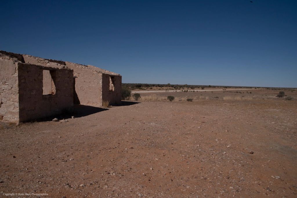 Ruins of a stone building in a vast arid landscape under a clear blue sky.