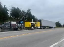 A yellow semi-truck with a large trailer parked on the roadside under a cloudy sky.