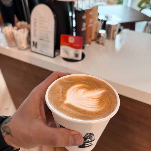 Main tenant une tasse de café latte avec art latte.