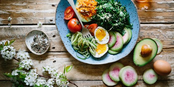 A fresh, healthy salad plate with eggs, avocado, and vegetables on a wooden table.