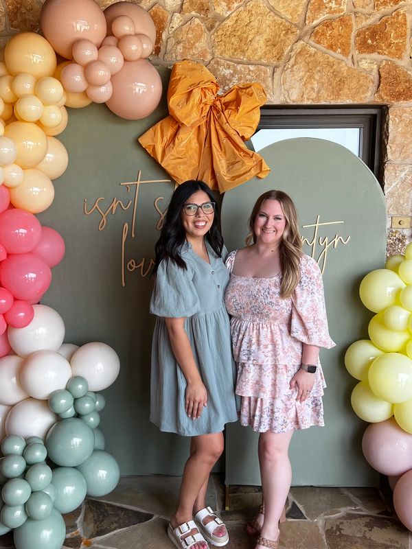 Two women posing in front of colorful balloon decorations and a stone wall.