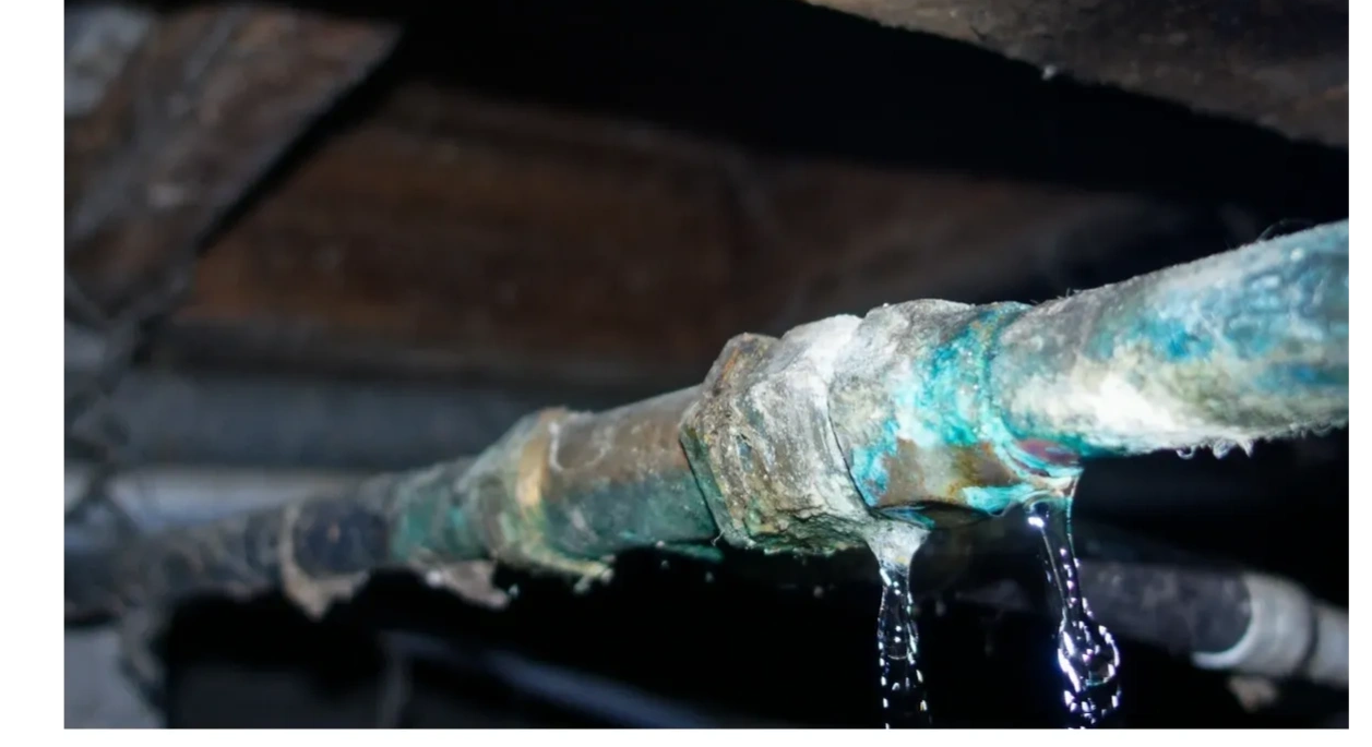 Corroded pipe leaking water drops in a dimly lit space.