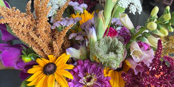 A vibrant bouquet with sunflowers, purple blooms, and assorted wildflowers.