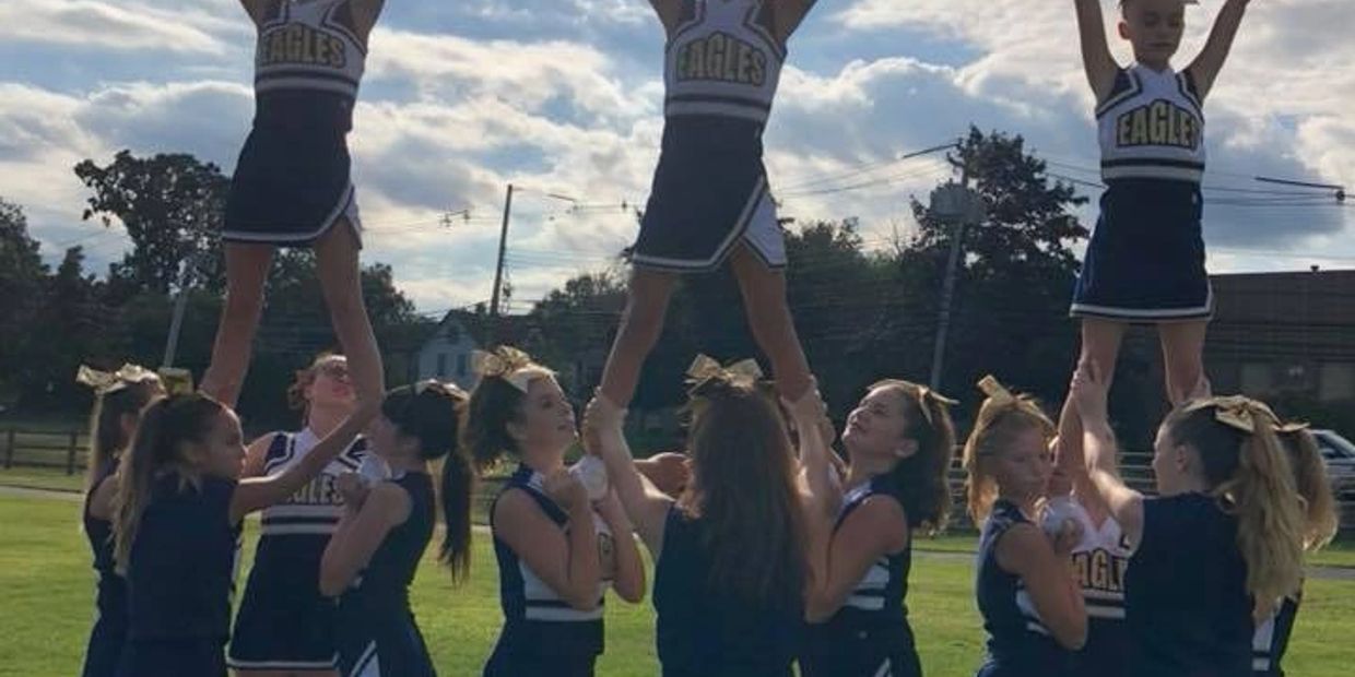 Cheerleaders performing a stunt outdoors in Eagles uniforms.