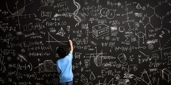 Little boy writing mathematical calculations on a blackboard 