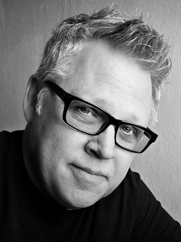 Black and white portrait of a man wearing glasses and a dark shirt.