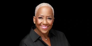 Smiling woman with short blonde hair against a black background.