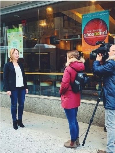 A woman is being interviewed on the street by a camera crew.