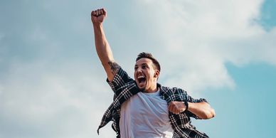 A young man excitedly jumping in to the air with a first above his head.