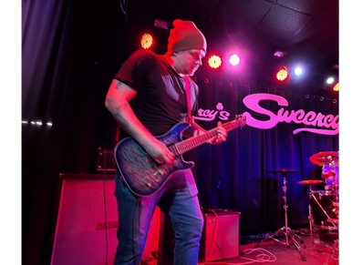 A musician passionately playing electric guitar on stage under colorful lights.
