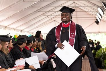Graduate smiling with diploma at ceremony.