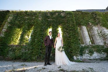 Bride and groom posing in front of a lush ivy-covered stone wall.