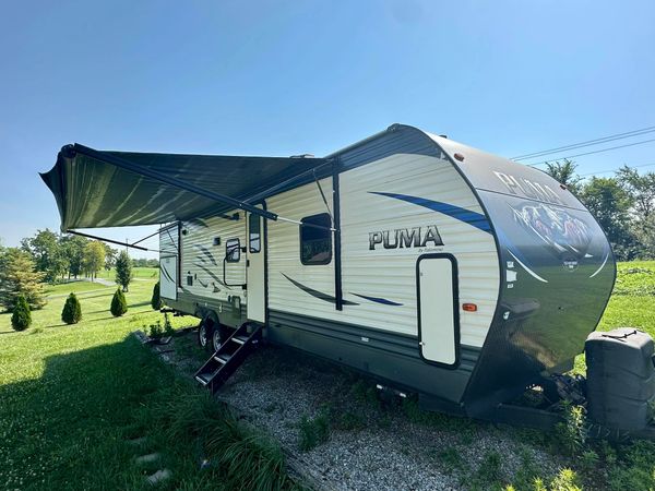 A Puma travel trailer parked on a grassy area with its awning extended.