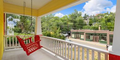 Porch with a red swing overlooking a street and greenery.