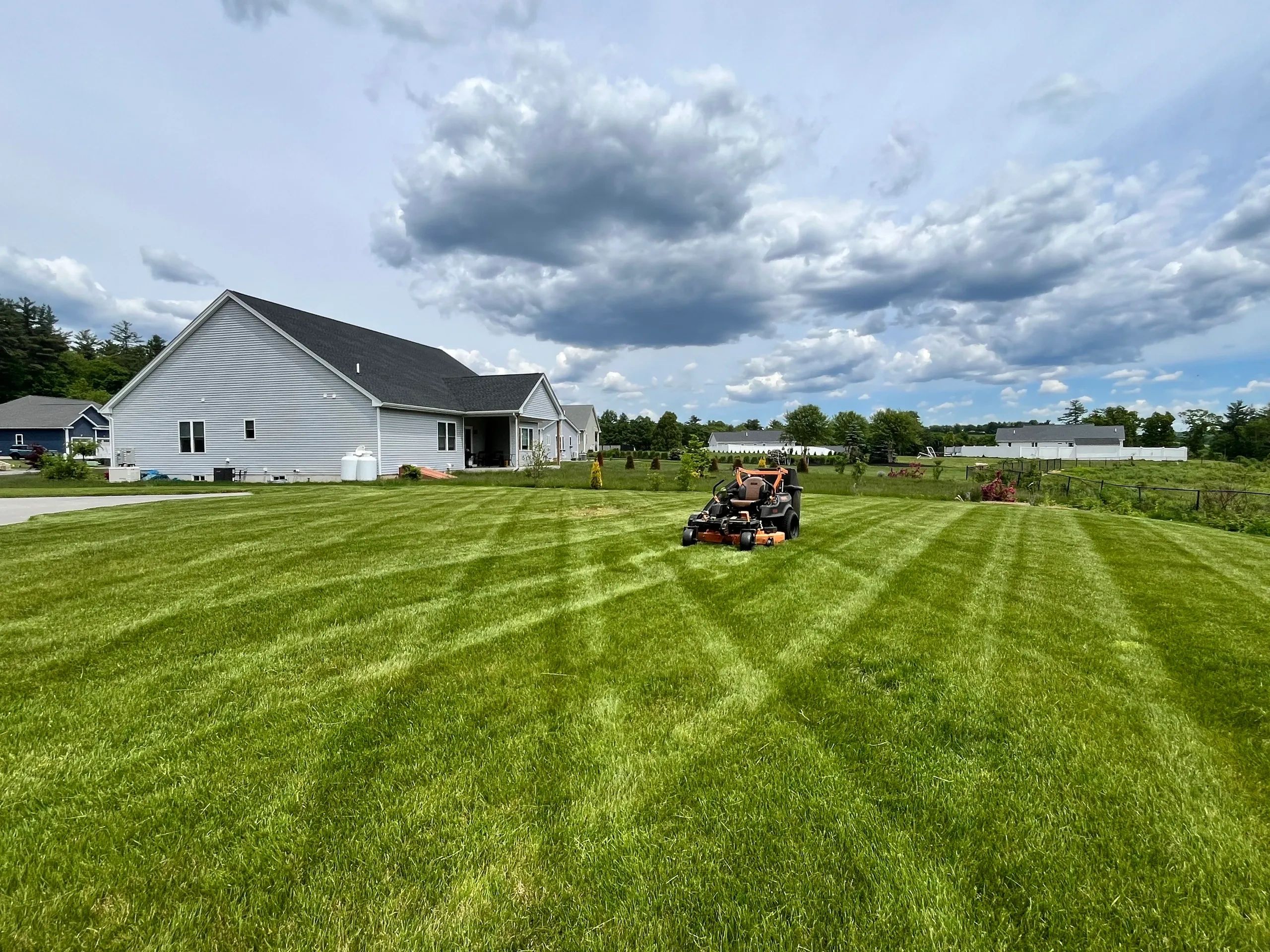 Mower on freshly cut lawn with clean stripes beside suburban houses under cloudy sky.