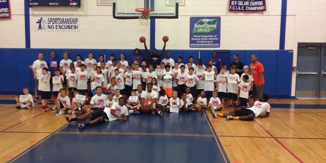 Large group of kids and coaches posing in a basketball gym with certificates and basketballs.