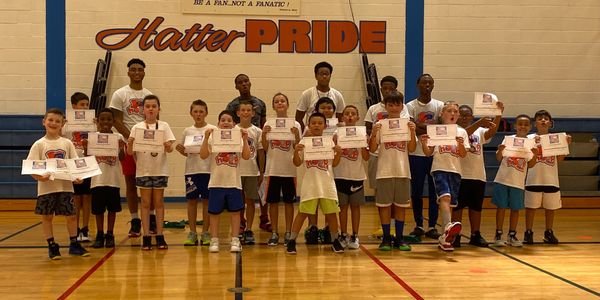 Group of children proudly holding certificates in a gym under 'Hatter Pride' banner.