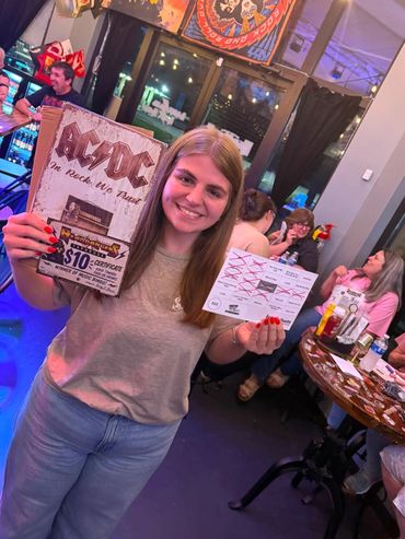 Woman smiling and holding an AC/DC-themed sign and a marked card.