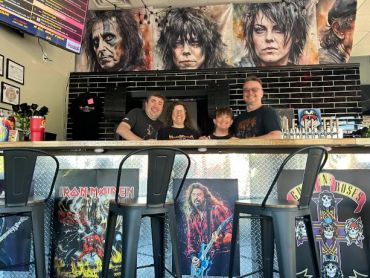 Group of four people behind a bar with rock band posters.
