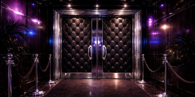Luxurious double doors with tufted black leather and metallic accents in a dimly lit hallway.