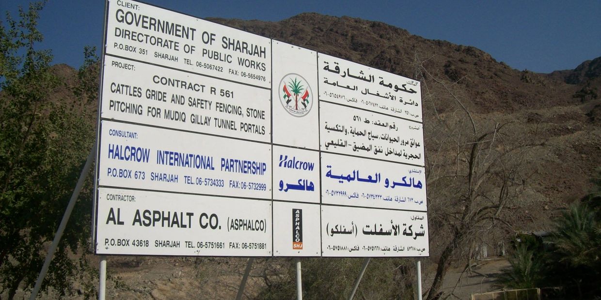 Construction project signboard by Government of Sharjah in a mountainous area.