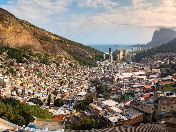 Dense urban area nestled between lush green hills and overlooking the ocean at sunset.