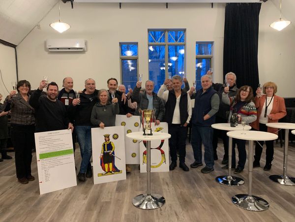 Group of people celebrating with a trophy and large playing cards indoors.