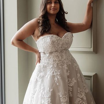 Woman in an elegant strapless lace wedding dress posing indoors.
