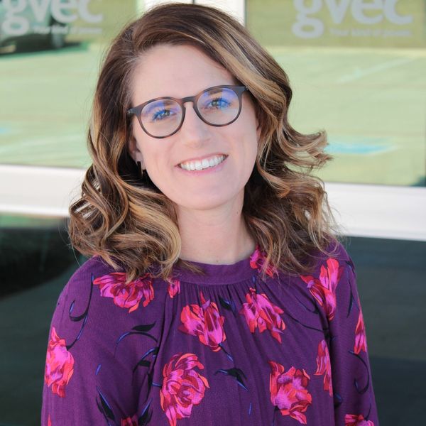 Smiling woman with glasses in a purple floral dress.