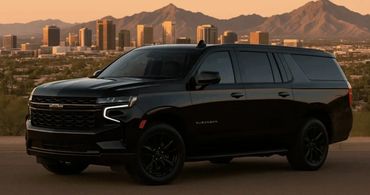 Black Chevrolet Suburban SUV parked with city skyline and mountains in the background.