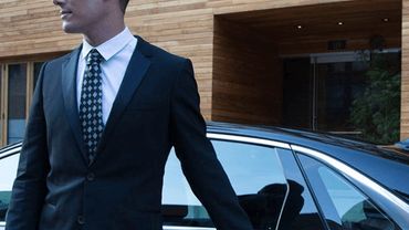 A man in a black suit opening a luxury black car door.