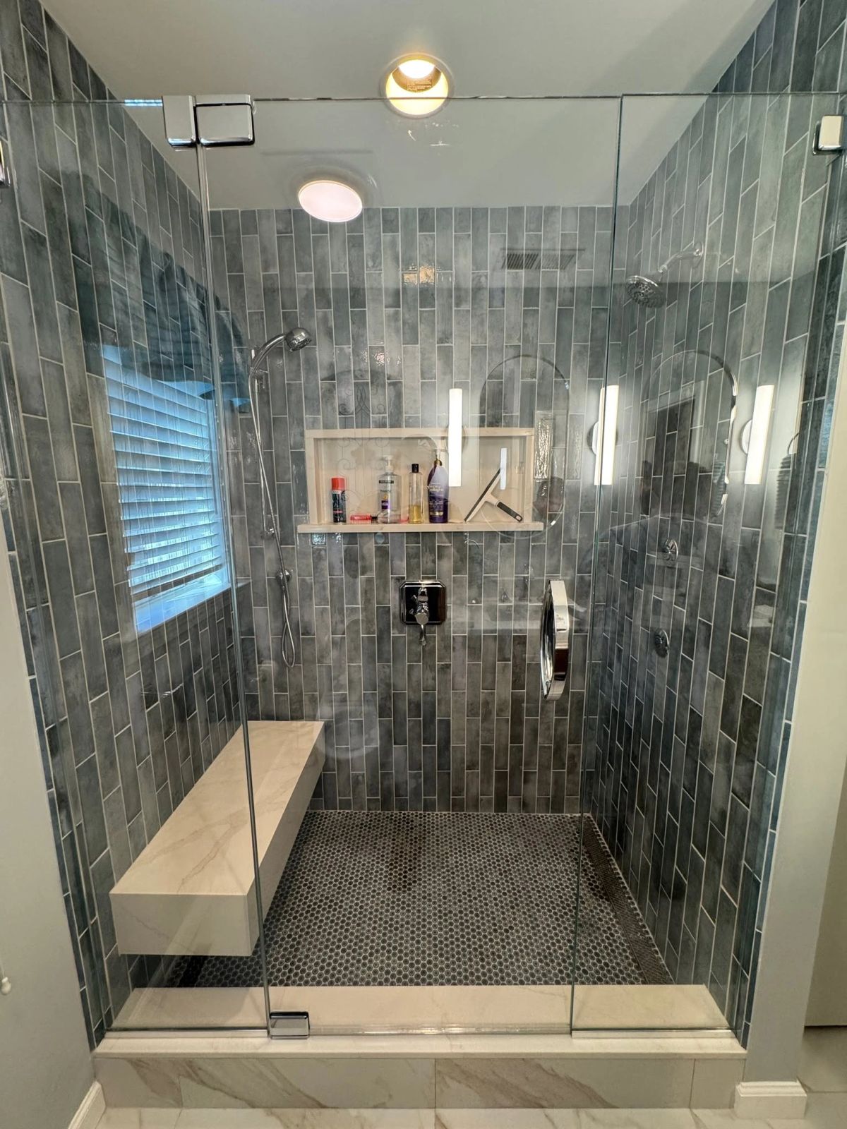 Walk-in glass shower with gray vertical tile, a recessed niche and a floating bench