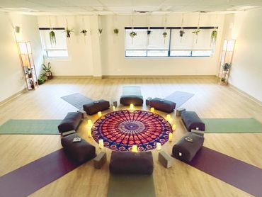 Peaceful yoga studio with mats, cushions, candles, and hanging plants arranged in a circular pattern.