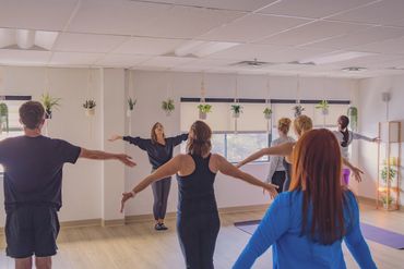 Group doing yoga or stretching in a bright room with hanging plants.
