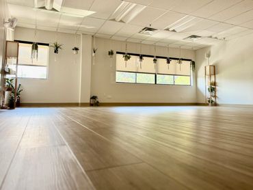 Sunlit empty room with wooden floor and hanging plants by the windows.