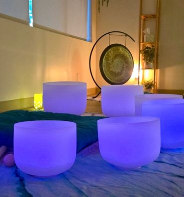 Glowing blue crystal singing bowls arranged in a serene space with a gong in the background.