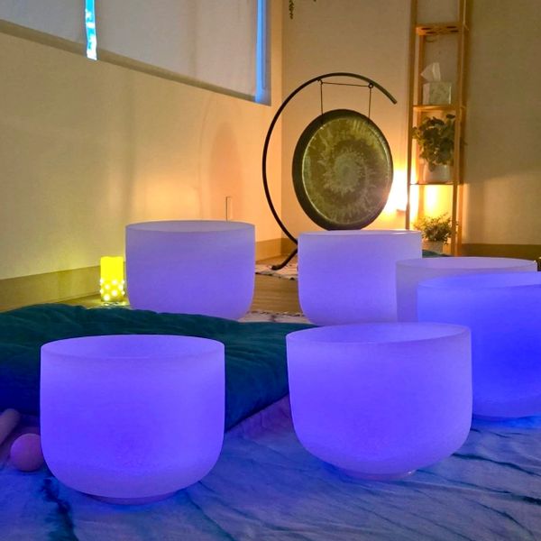 Glowing blue crystal singing bowls arranged in a serene space with a gong in the background.