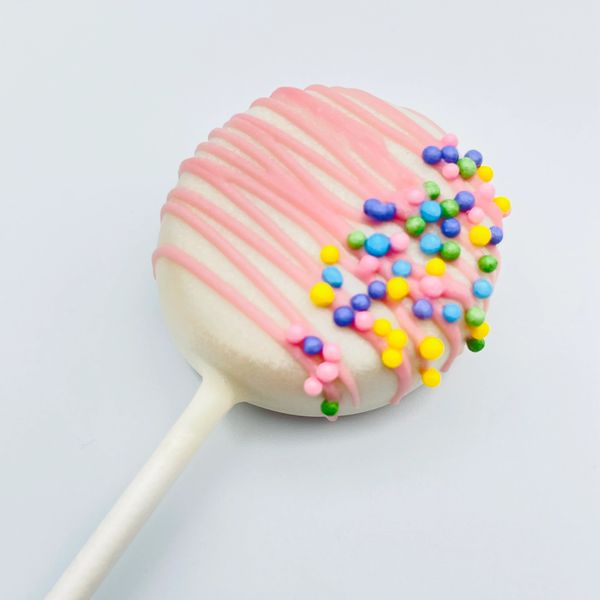 White cake pop with pink drizzle and colorful sprinkles.