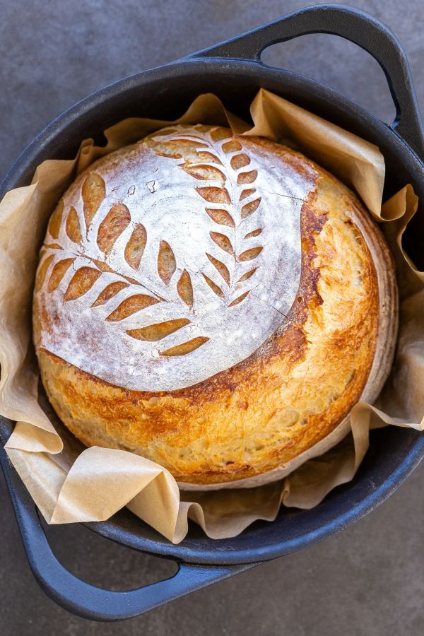 Freshly baked artisan bread with a decorative leaf pattern in a cast iron pot.