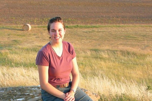 A woman sitting on a rock in a grassy field with a smile.
