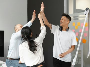 Three colleagues enthusiastically give high-fives in a modern office setting.