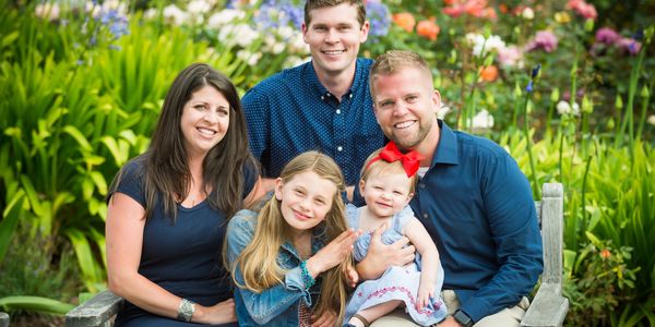 A happy family of five sitting on a bench surrounded by colorful flowers.