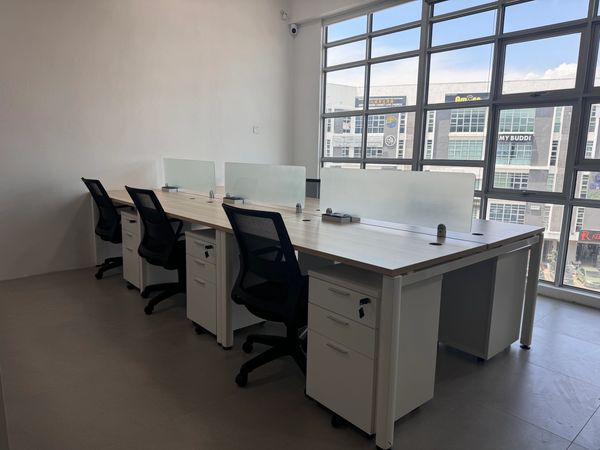 Modern office workspace with black chairs and light wood desks near large windows.