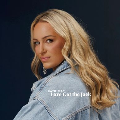 Blonde woman in a denim jacket posing against a dark background.