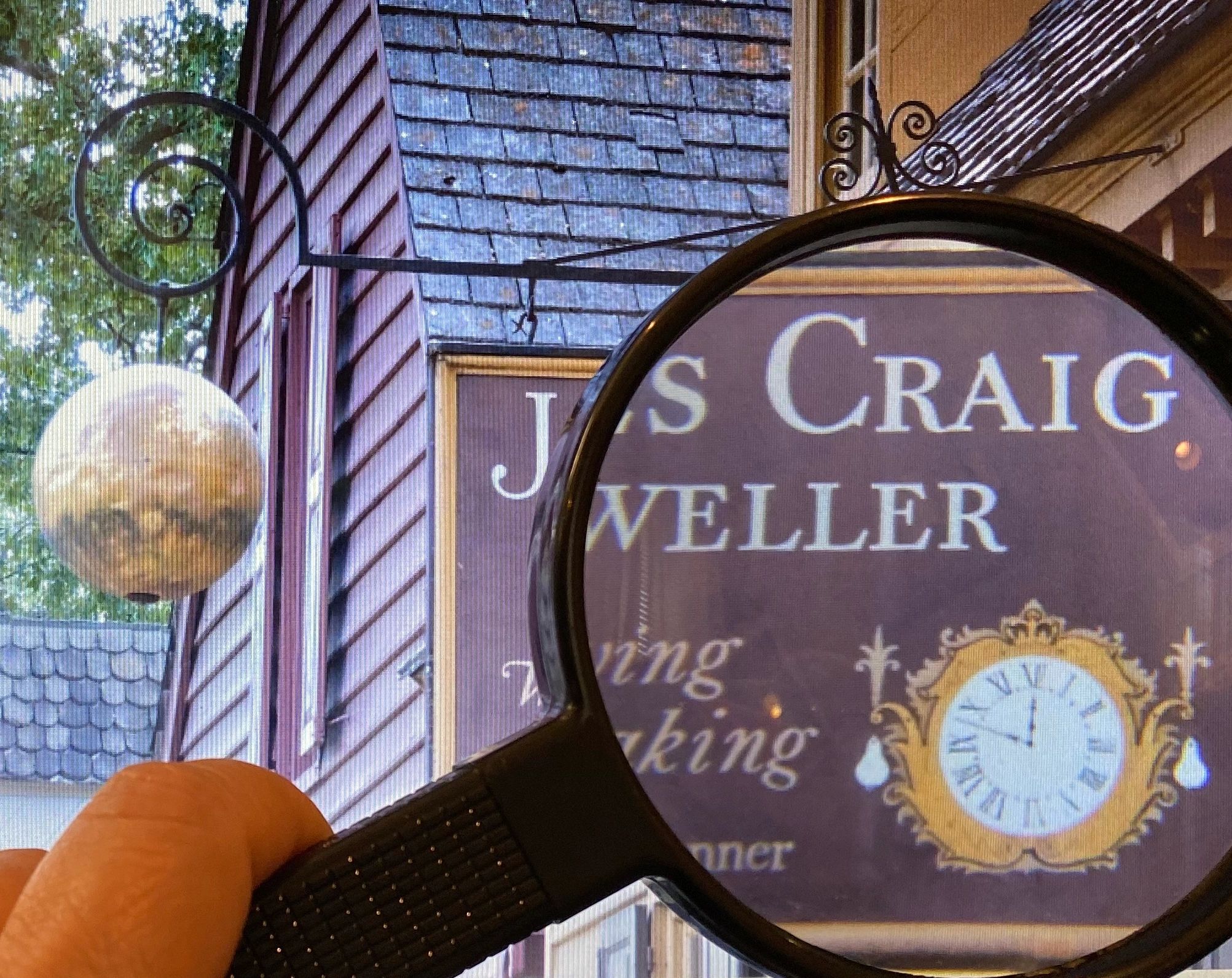 Magnifying glass showing close up of the  clock on James Craig Jeweler's store sign in Williamsburg 